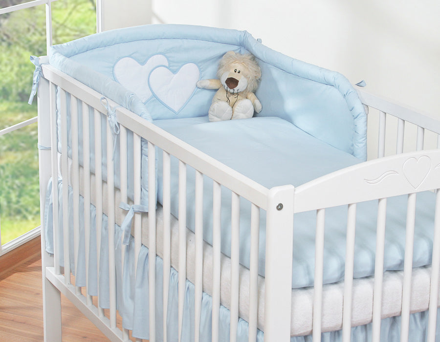 White crib with blue bedding and a teddy bear, surrounded by greenery