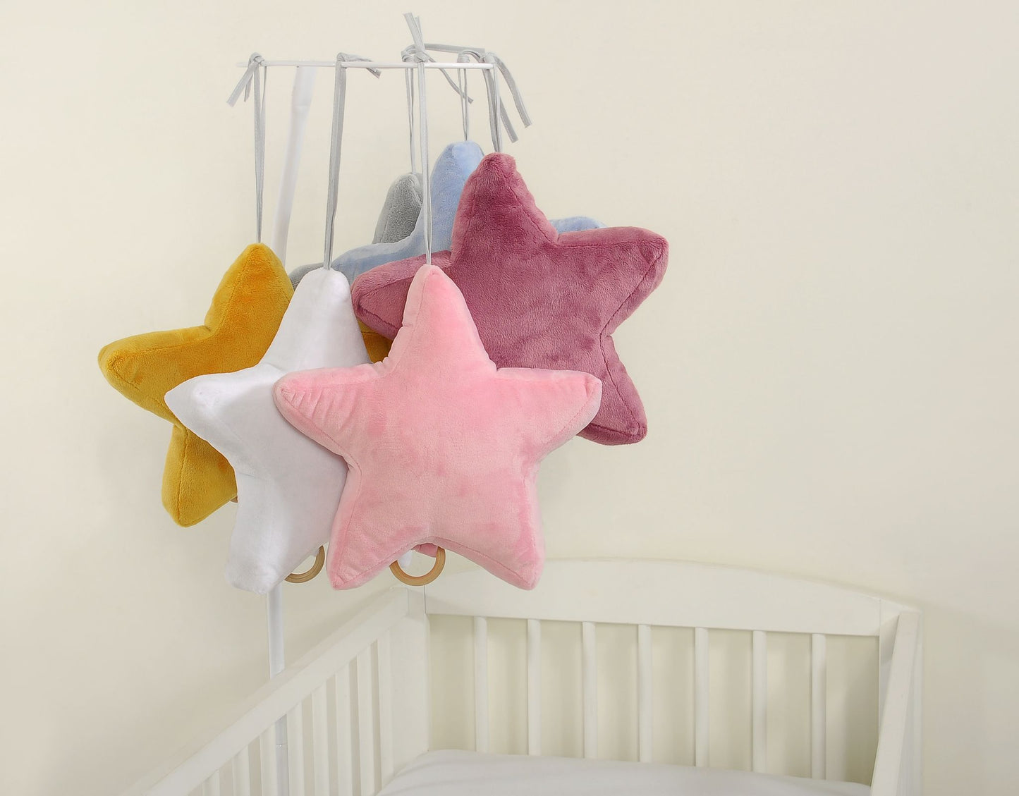 Colorful star-shaped pillows hanging above a crib against a plain wall.
