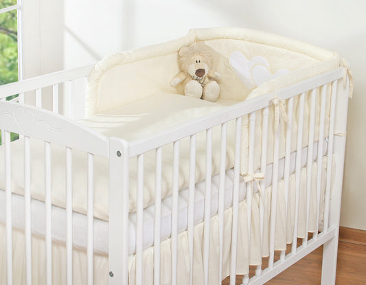 White crib with a teddy bear and white comforter in a bright room.