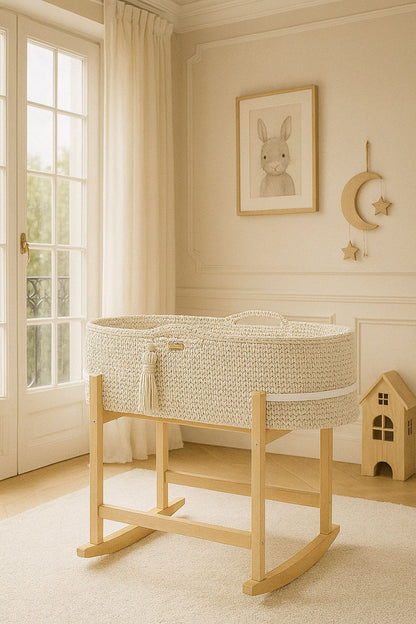 Nursery with a woven crib on a wooden stand, framed picture of a rabbit, and decorative moon and star wall hanging.